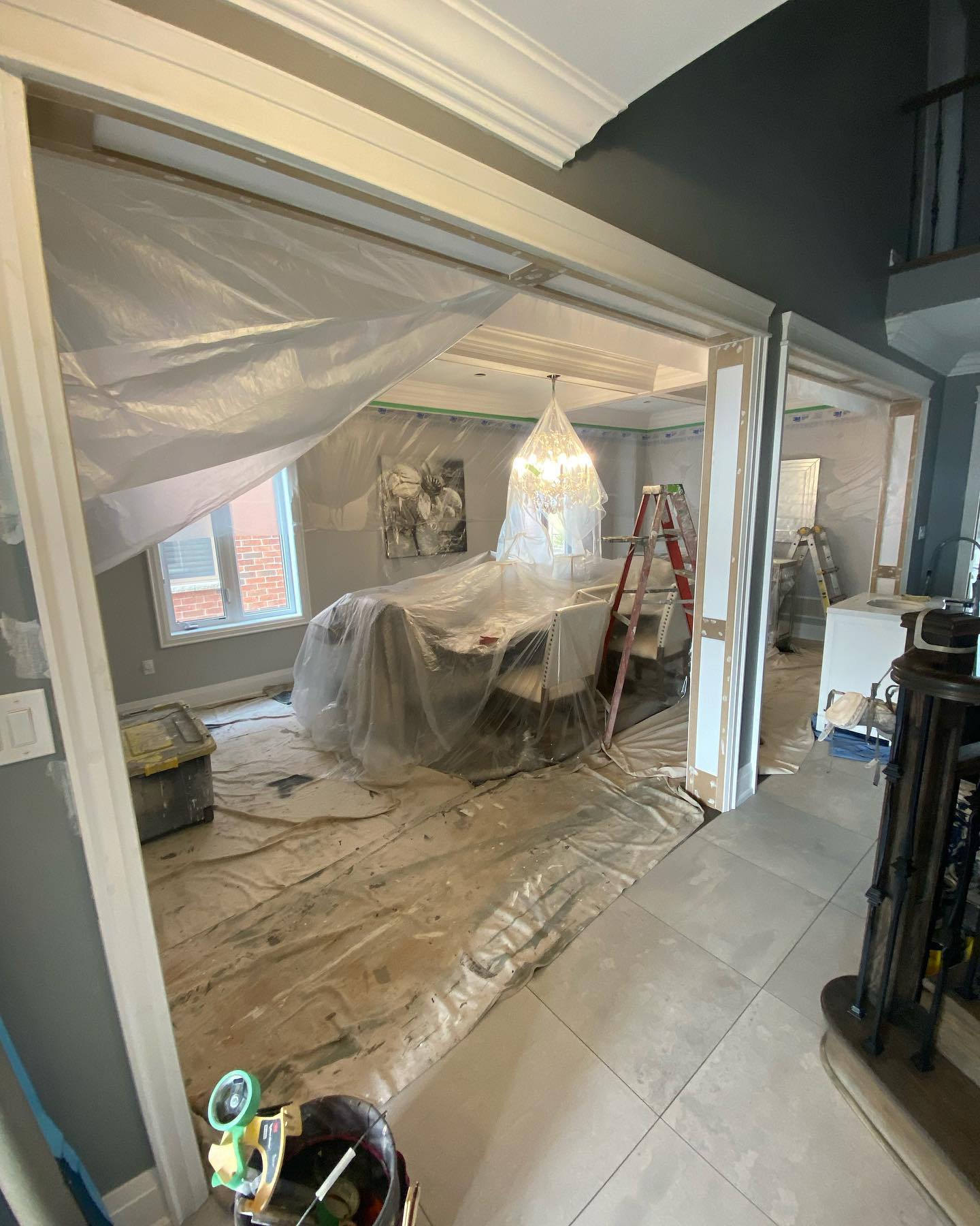 Dining room with plastic sheeting over furniture and ceiling beams being prepped