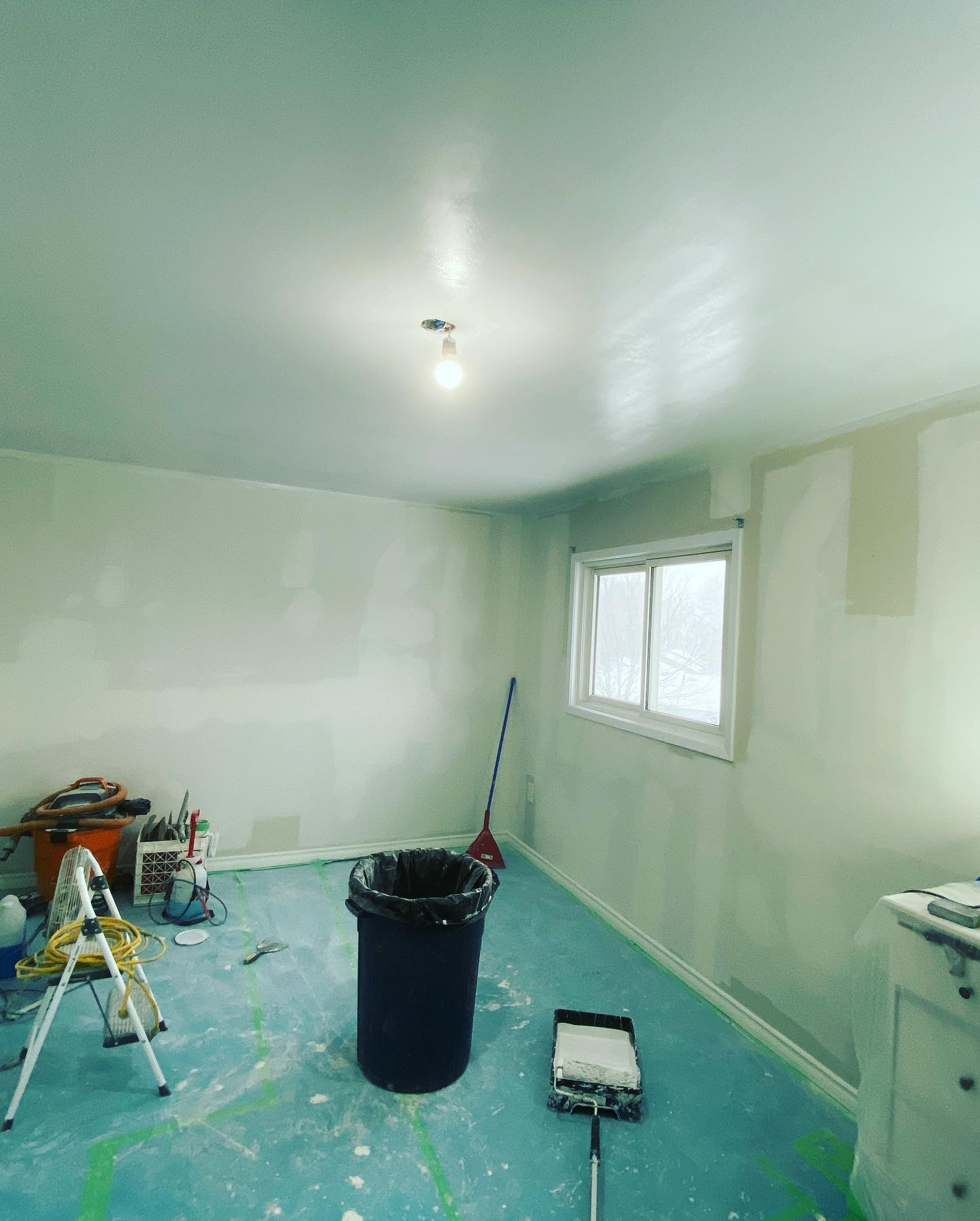 Room with freshly primed ceiling and walls, floor covered, ladder and paint tray