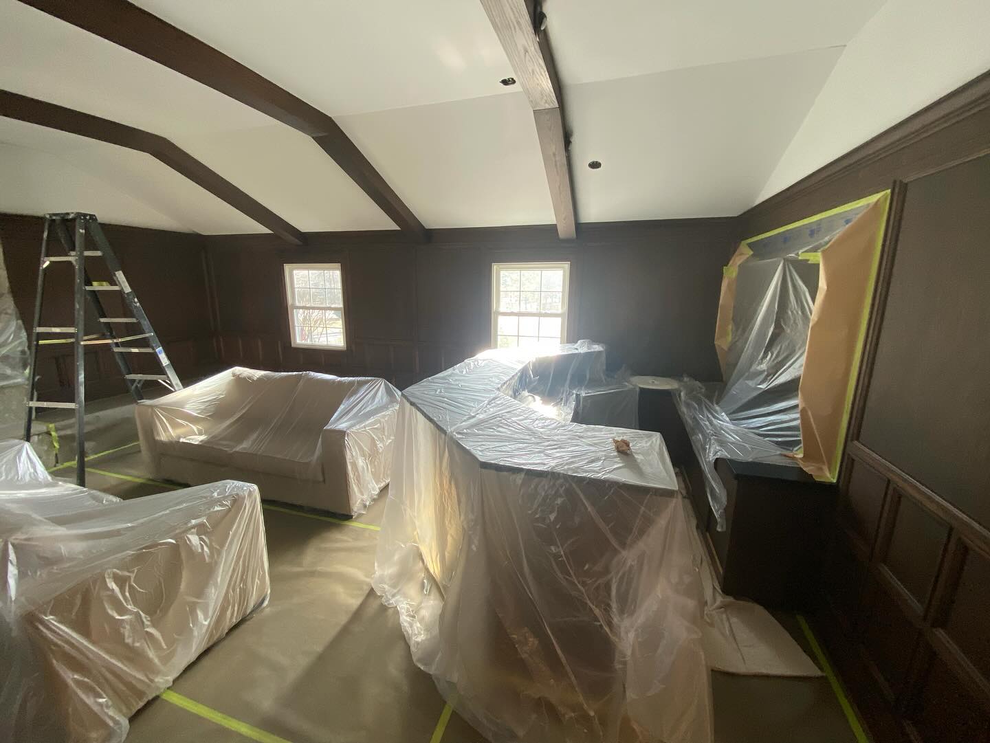 Vaulted room with exposed dark beams and furniture covered in plastic