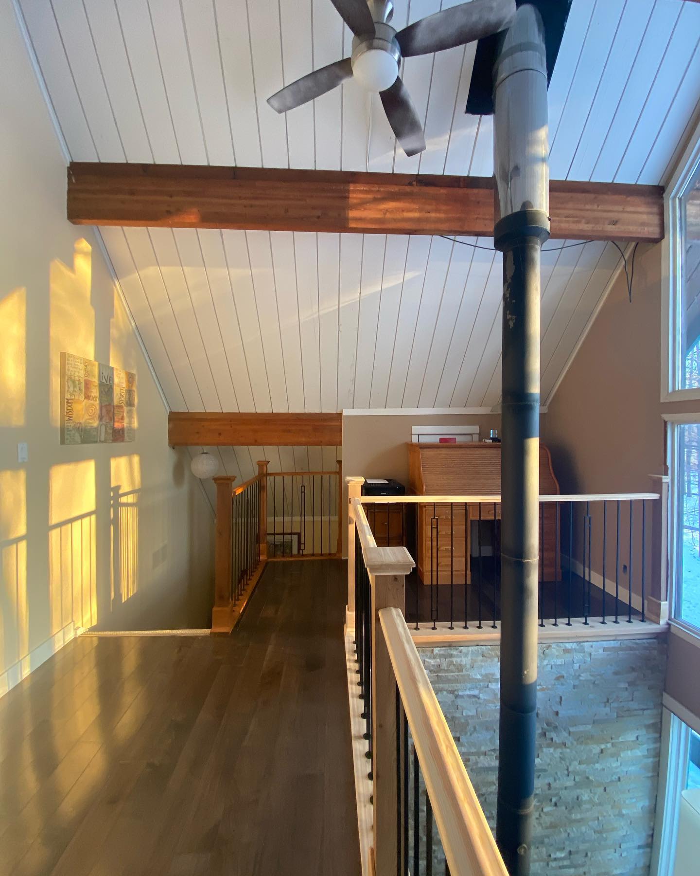 Vaulted ceiling with a dark wood beam and fan above a balcony railing