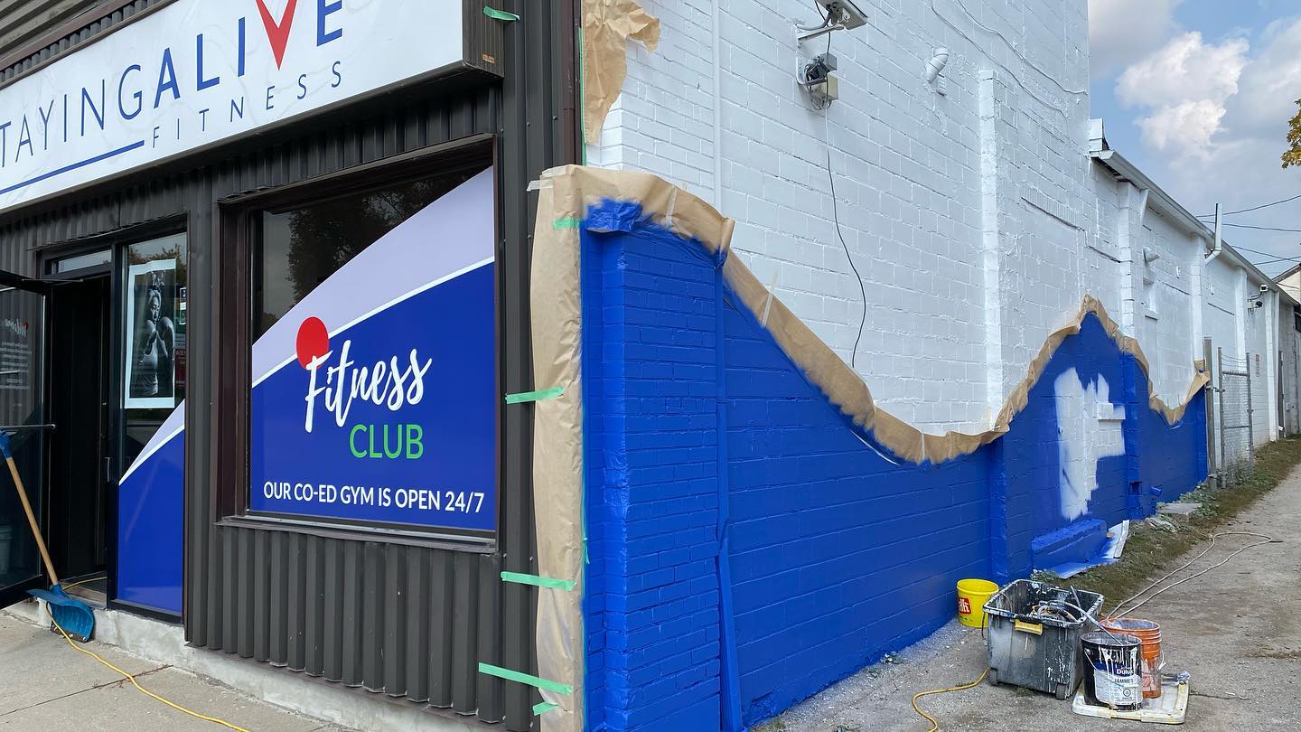 Storefront exterior with blue paint being applied to a brick wall, partly done