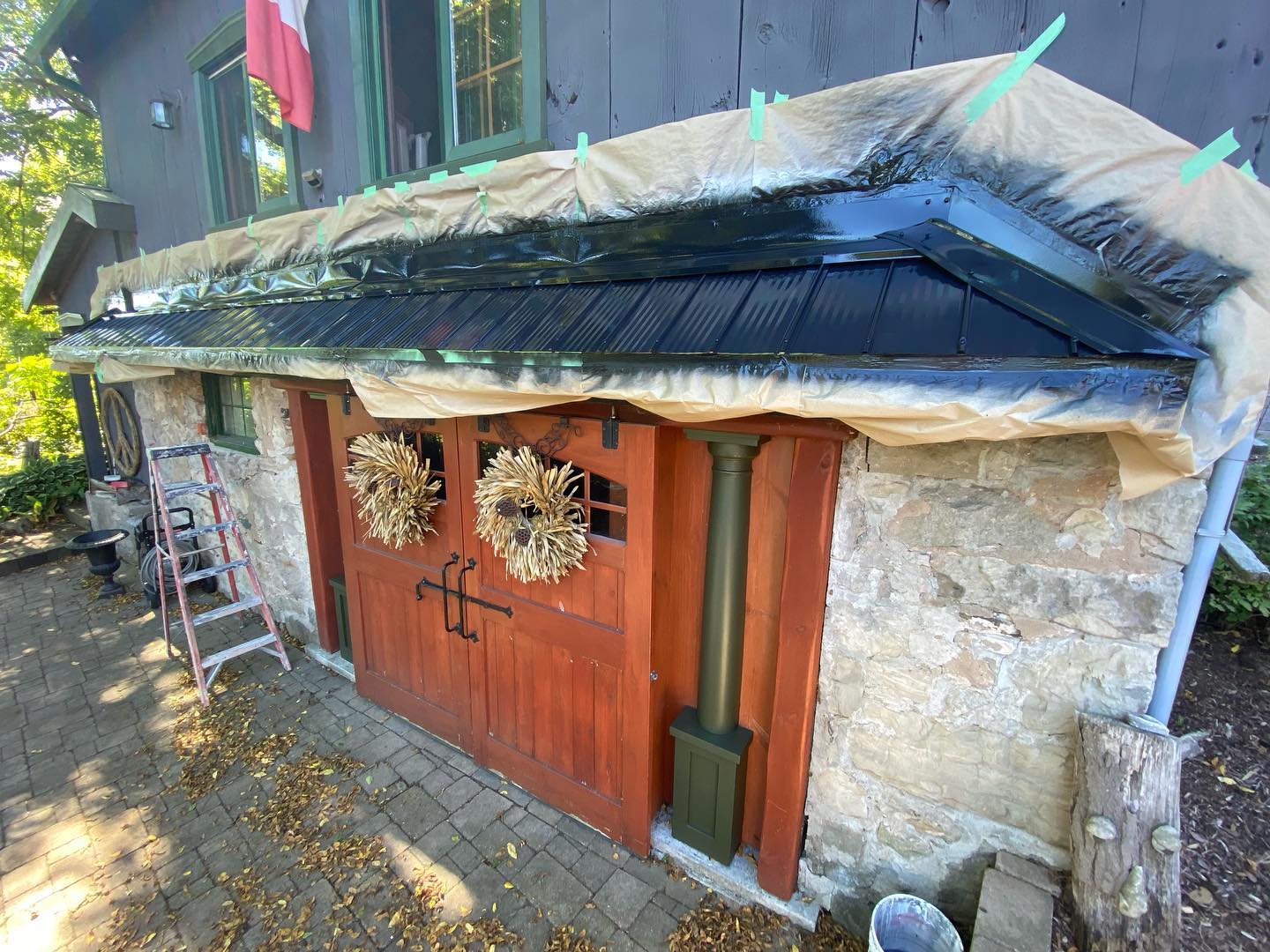 Red-brown carriage doors and trim on a stone outbuilding with the roof masked