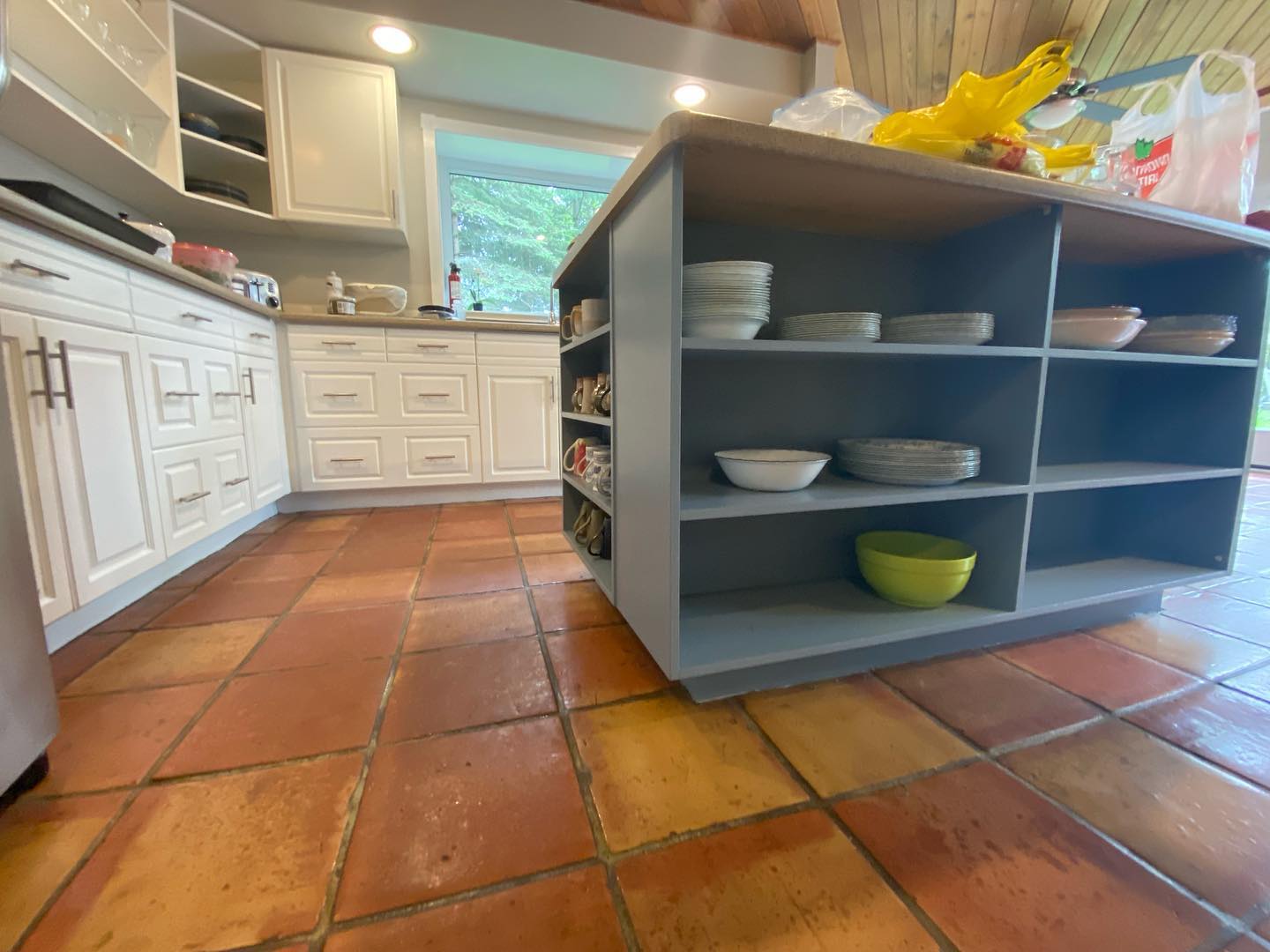 Open shelf island in grey-blue beside white kitchen cabinets