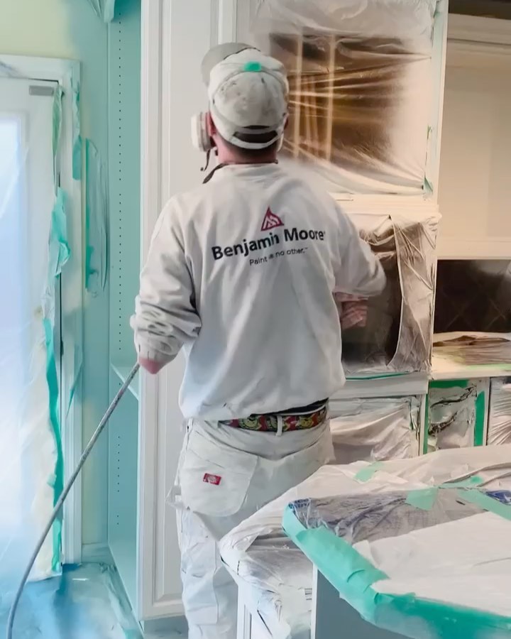 Painter in a mask spraying a cabinet with the room masked off