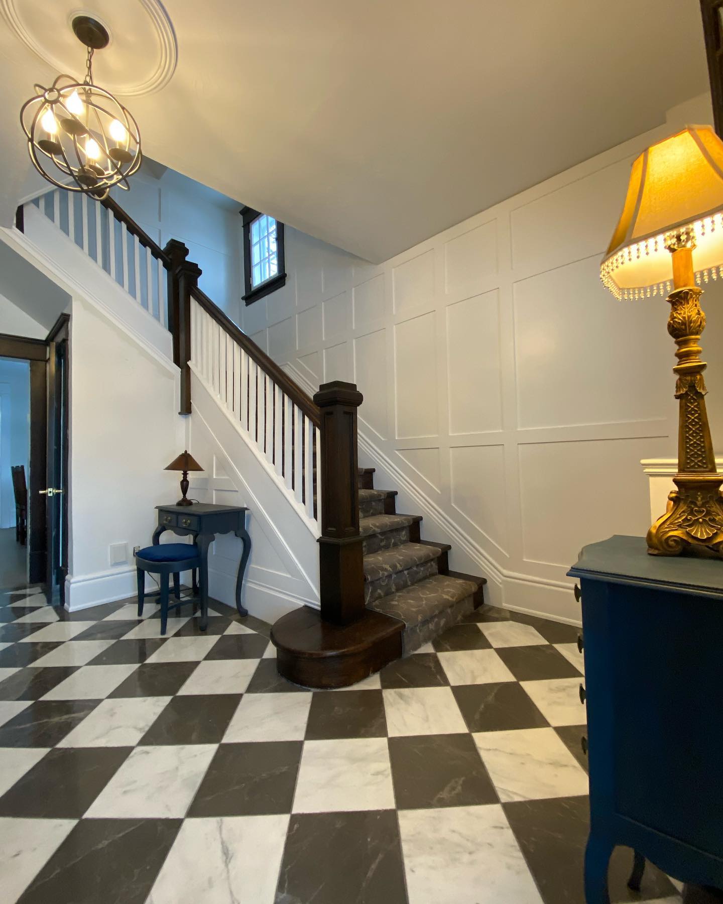 Foyer with white wainscoting, painted stair spindles and black and white tile