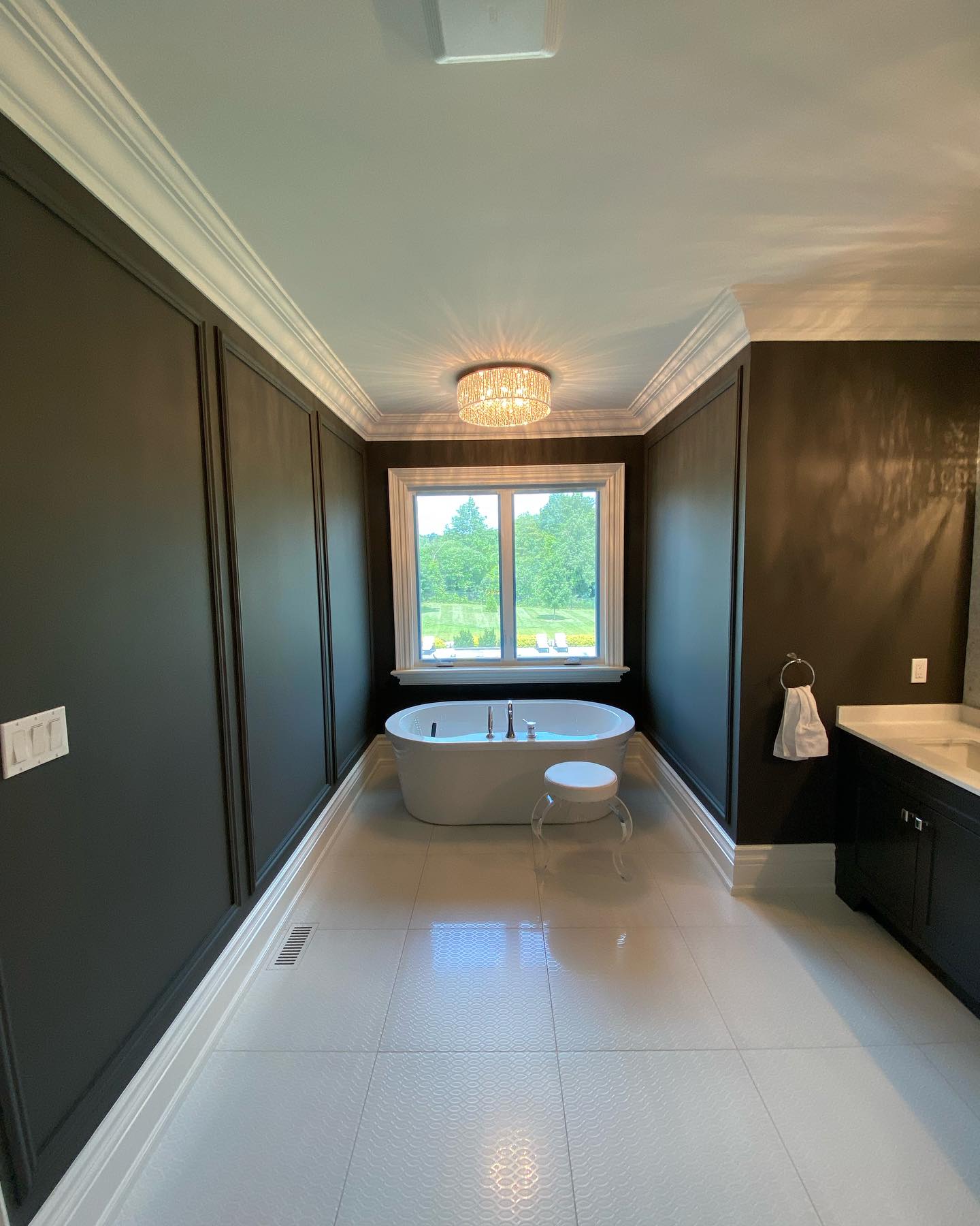 Dark painted bathroom walls with a freestanding tub and bright window