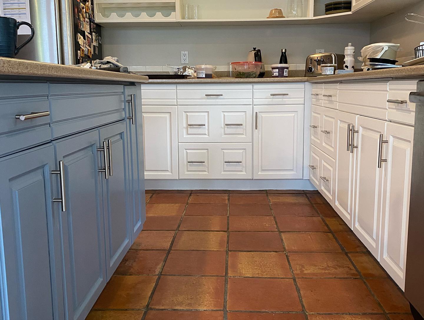 Kitchen with grey-blue lower cabinets and white upper cabinets on terracotta tile