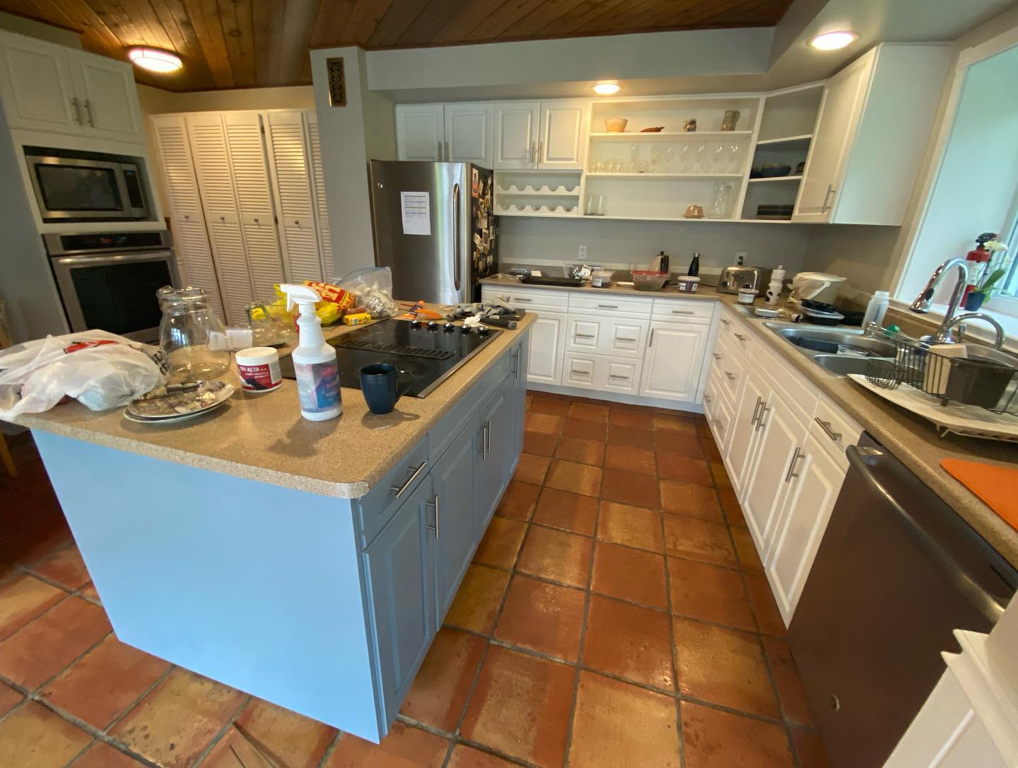 Kitchen island in grey-blue with white perimeter cabinets and wood ceiling